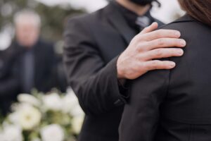 Funeral, support and people care for grief, mourning or depressed mother at burial ceremony, memorial service or cemetery. Hand, shoulder and man helping sad woman with love, advice or family comfort